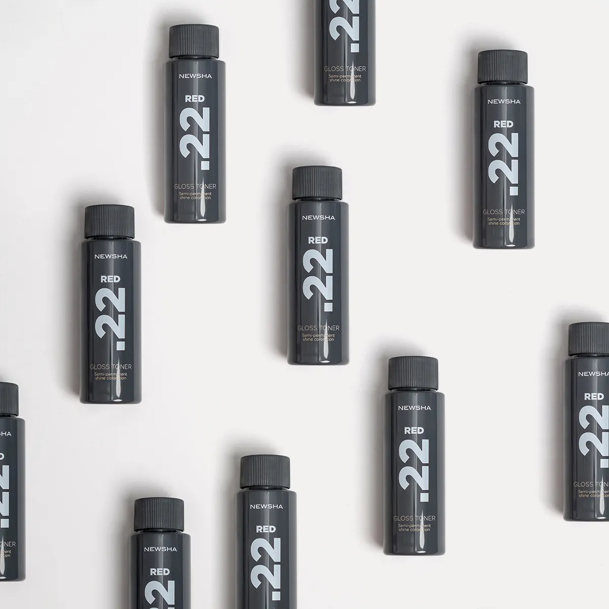 Mehrere schwarze Flaschen des NEWSHA Gloss Toner Red .22 f&uuml;r professionelle Haarcoloration und gl&auml;nzende rote Haarfarben auf hellem Hintergrund.