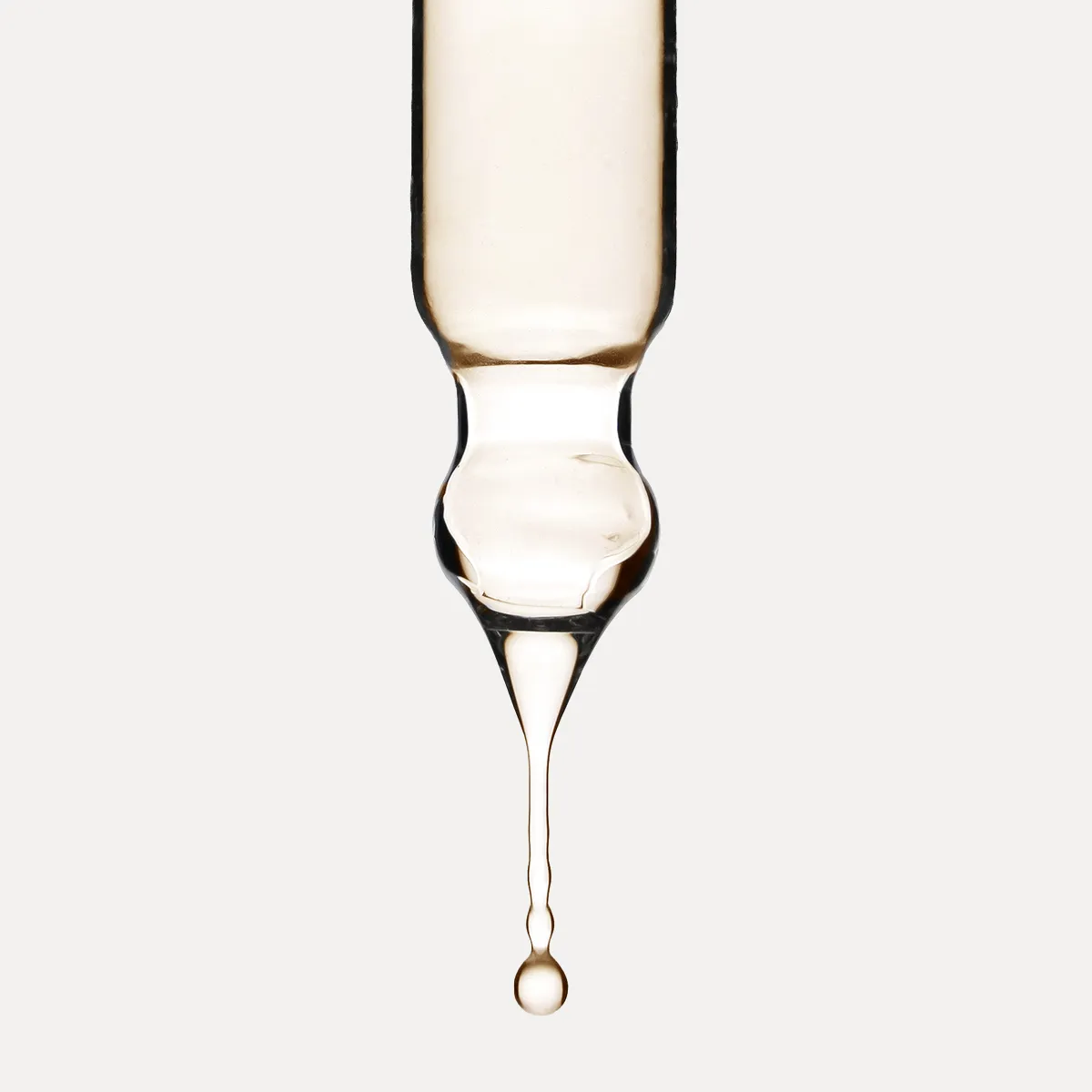 Nahaufnahme einer Glaspipette mit einem Tropfen transparenter, leicht goldener Fl&uuml;ssigkeit als Symbol f&uuml;r professionelle Haarpflege.