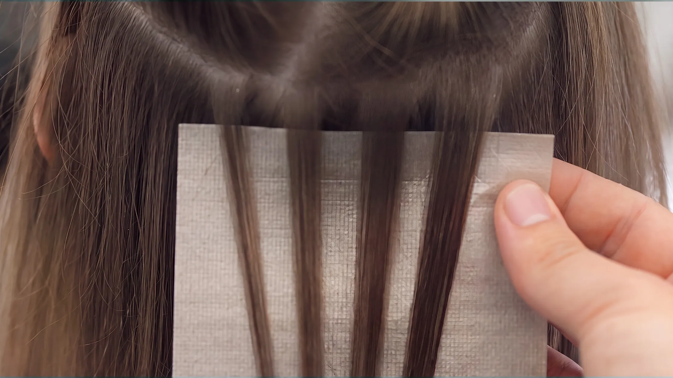Nahaufnahme einer professionellen Haarcoloration: Eine Hand hält Alufolie an feine braune Haarsträhnen, um die Haarcoloration aufzutragen.