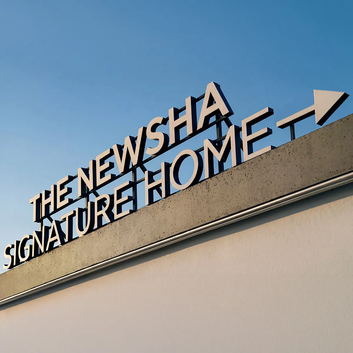 NEWSHA Schriftzug „The NEWSHA Signature Home“ auf dem Dach eines modernen Gebäudes vor blauem Himmel als Symbol der Markenidentität.